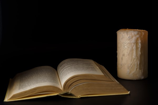 Large book illuminated by the light of a white candle