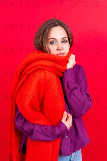 Beautiful young woman with warm red scarf on red background. cold winter portrait
