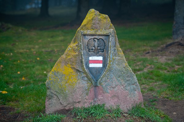 A large obelisk is placed next to the tourist trail with a trail sign and an eagle on it. Polish mountains