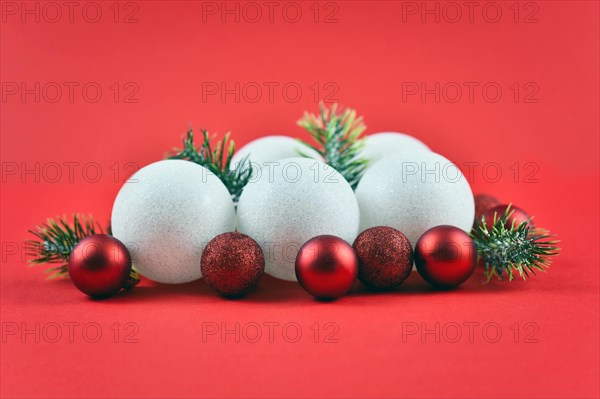 Pile of traditional white and red Christmas tree ornaments baubles and pine branches on red background
