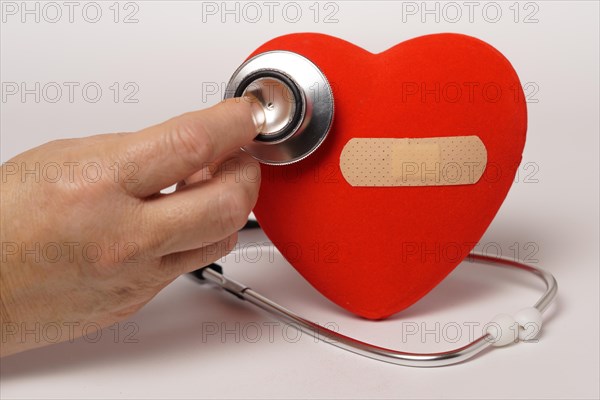 Woman auscultating a red heart with a band-aid with a stethoscope isolated on a white background