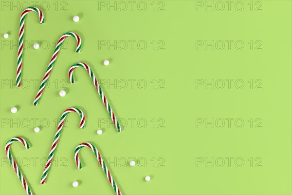 Striped candy cane Christmas sweets with snowballs on side of green background with copy space