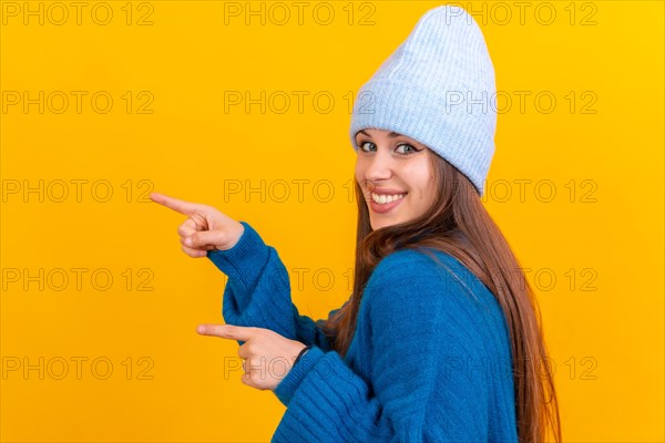 Attractive woman smiling pointing fingers at copy space on yellow background