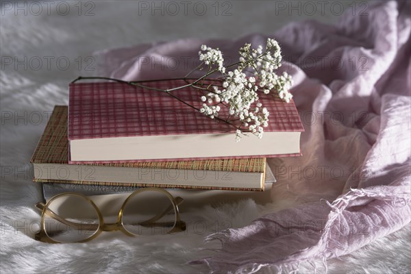 Three closed books with glasses and babys breath on white fur with pink cloth