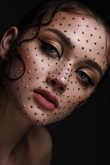 Beautiful woman with creative hairstyle and makeup with rhinestones. Beauty face. Photo taken in the studio