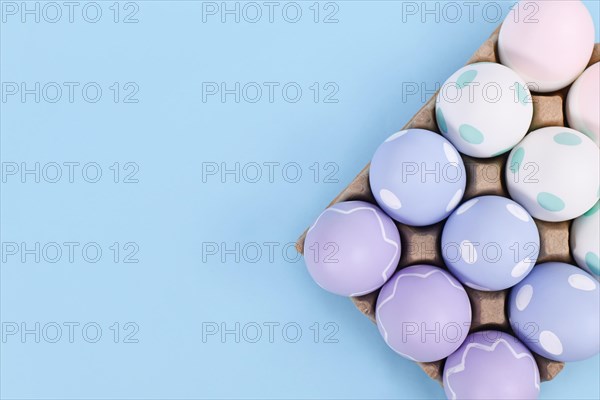 Box of pastel colored easter eggs on blue background with copy space