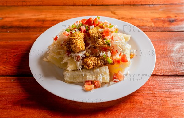 Traditional chicharron dish with cassava and tomato salad. Latin food chicharron con yuca served on wooden table. Nicaraguan dish chicharron with cassava on the table