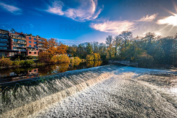 The Leineinsel waterfall next to the Leineinsel residential area in the district of Doehren in autumn with veil clouds