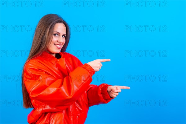 Attractive woman smiling pointing fingers at copy space on blue background