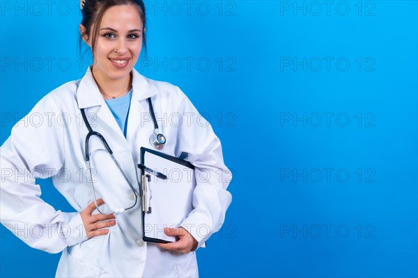 Portrait of smiling female doctor in medical gown standing isolated on blue