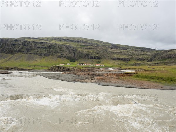 Glacier river and farm in front of mountain range