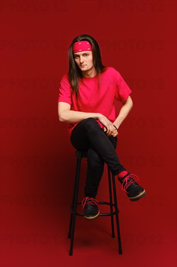 Young adult man sits on high stool with his leg on another leg and leaning forward