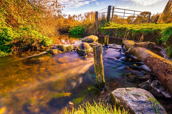 Long exposure of a small river next to a pasture with stones in the riverbed