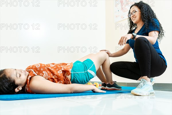 Physiotherapist with patient on the floor doing knee rehabilitation exercises. Woman physiotherapist assisting patient lying down doing exercises on the mat