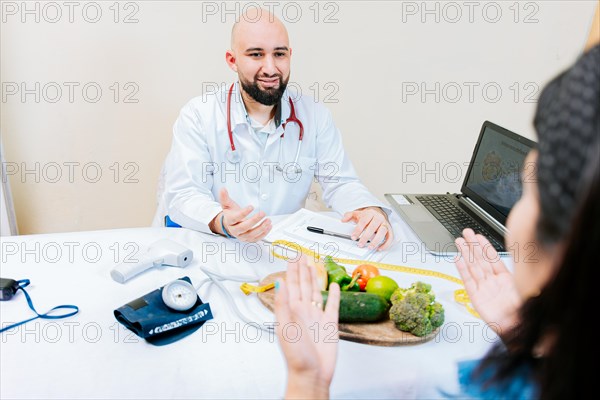 Nutritionist man talking to woman patient in office. Back view of a female patient talking to the nutritionist. Smiling nutritionist explaining to a female patient