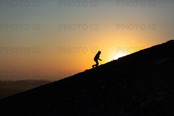 Silhouette of man is climbing to peak of hill with sunset or sunrise background. Poland