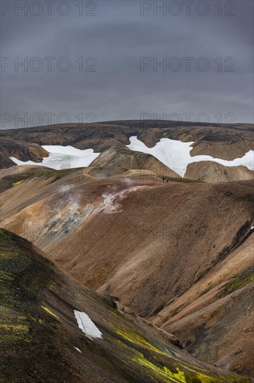 Hikers on colourful rhyolite mountains with remnants of snow