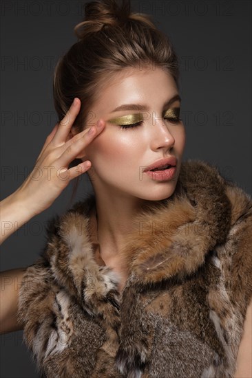 Portrait of a beautiful woman in a furcoat with creative gold makeup in a fashion style. Beauty face. The photo was taken in a studio on a black background