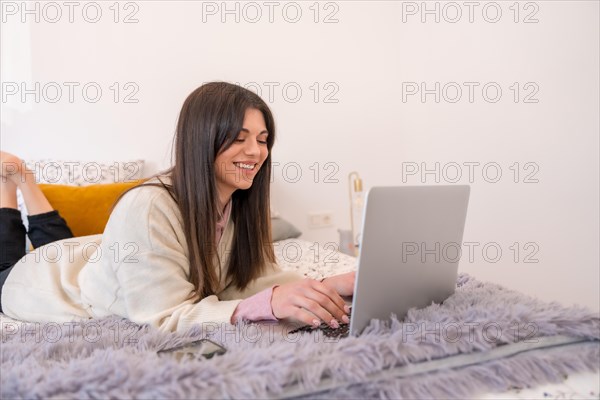 Young woman working with laptop in bed