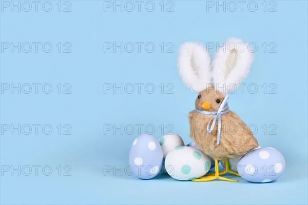 Easter chick with bunny ears and pastel Easter eggs on blue background with copy space