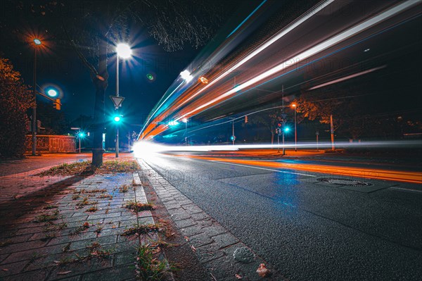 Long exposure of moving cars on a road just in front of an intersection with traffic lights at night with lanterns lit