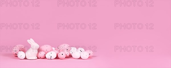 Banner with white and pink Easter eggs with small bunny sculpture on pink background with copy space
