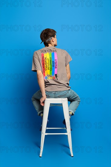Unrecognizable adult person sits on tall stool in t-shirt with rainbow flag printed on back side. Concept of tolerant attitude to lgbt people