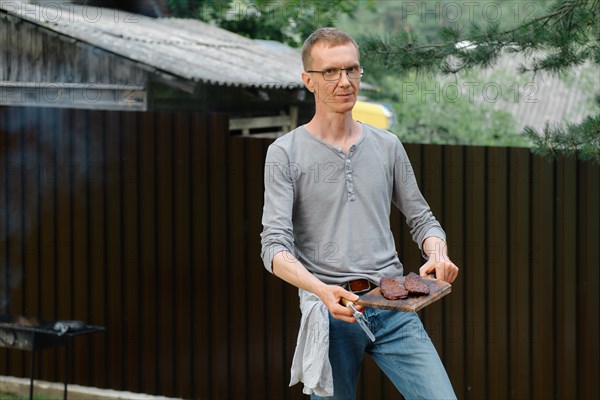 Satisfied middle-aged man with beef steak cooked on the grill in the backyard of country house