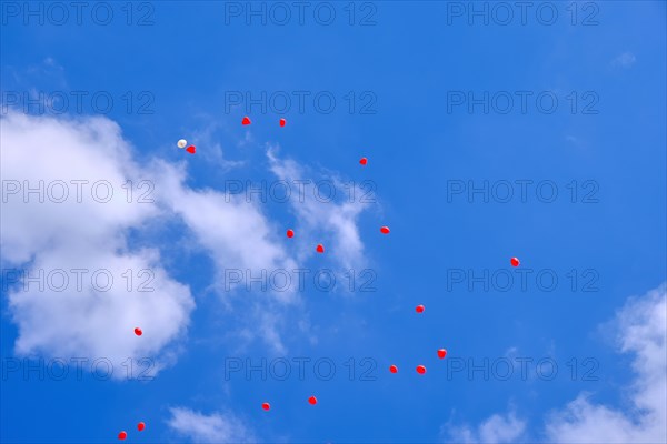 Heart-shaped balloons rise into the blue cloudy sky