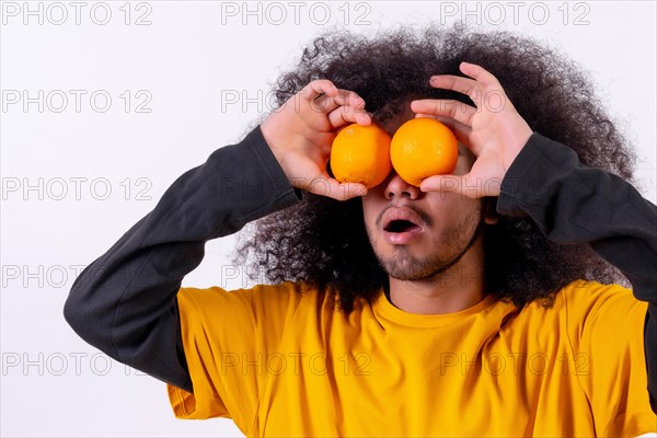 Portrait with the orange fruit in the eyes with an open mouth. Young man with afro hair on white background