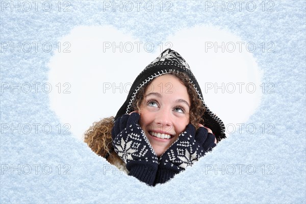 Woman looking through a snow heart on a window pane