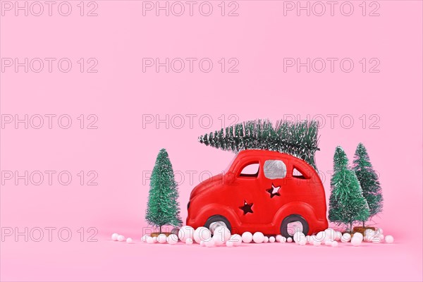 Miniature red car transporting christmas tree on pink background