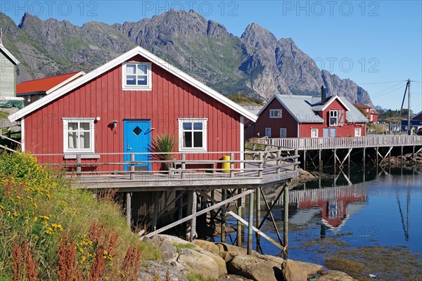 Wooden houses on stilts by a fjord are reflected in the calm waters of a fjord