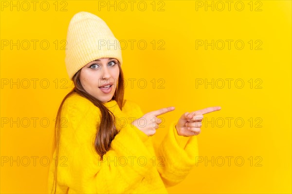 Attractive woman smiling pointing fingers at copy space on yellow background