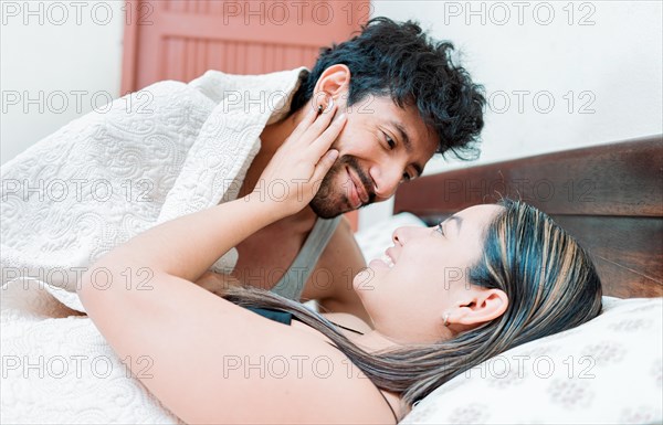 Man waking up woman with a kiss in bed. Couple in love in bed looking at each other with love