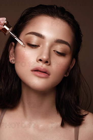 Beautiful young girl with natural nude make-up with cosmetics oil in hands. Beauty face. Photo taken in studio