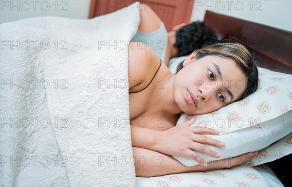 Upset couple sleeping on their backs. Young couple arguing and sleeping apart. Concept of couple problems in bed. Unhappy couple in bed sleeping apart