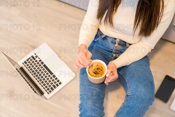 Hands of a woman with a computer sitting on a sofa with a hot coffee