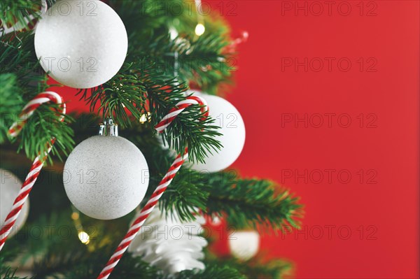 Close up of decorated Christmas tree with white and red seasonal tree ornaments like baubles and candy canes on red background