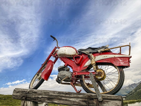 An old rusty red motorcycle stands on a wooden pole