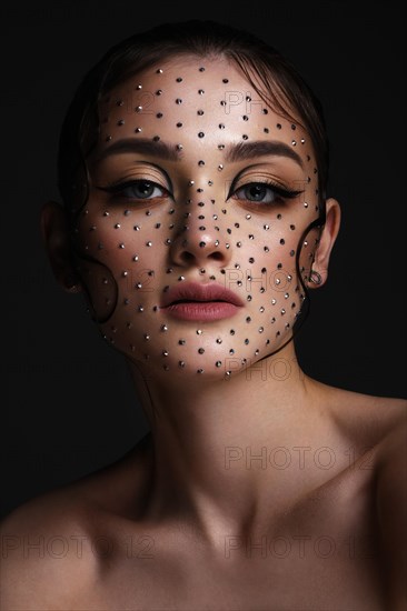 Beautiful woman with creative hairstyle and makeup with rhinestones. Beauty face. Photo taken in the studio