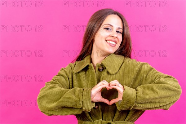 Young brunette woman wearing green sweater over isolated pink background smiling in love making heart symbol shape with hands. romantic concept