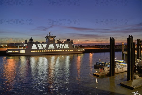 Illuminated island ferry in front of sunrise in the harbour of Norddeich