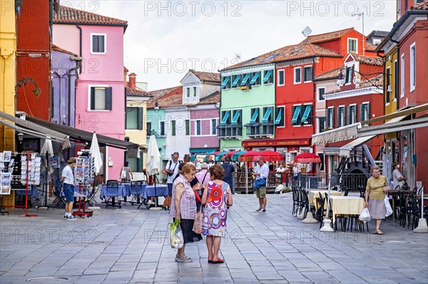 Elderly local women shopping at square with brightly coloured restaurants at Burano