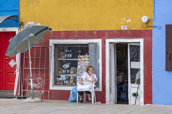 Elderly female shopkeeper waiting in front of her colourful shop at Burano