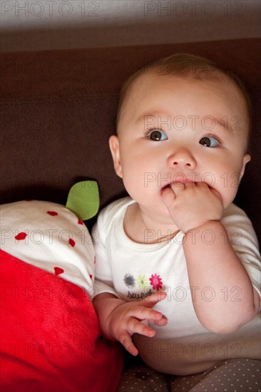 Sitting baby girl with her hand in her mouth
