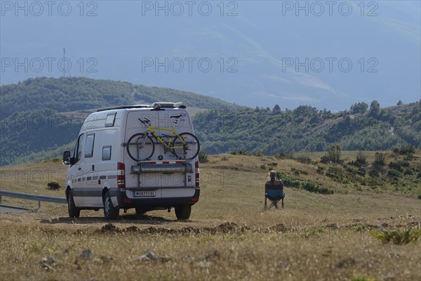 Woman sitting by the camping bus in a meadow