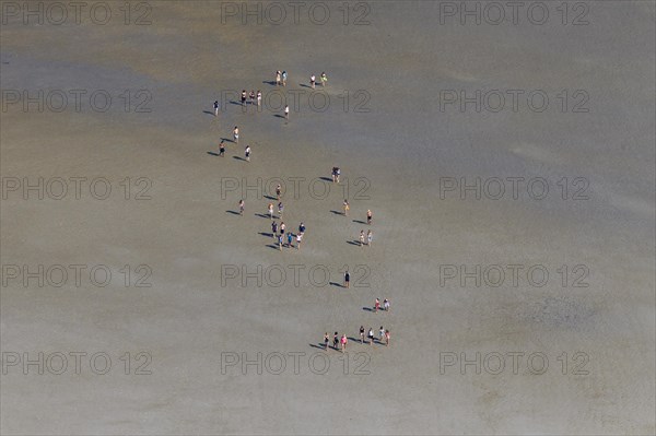 Aerial view over group of tourists walking with guide during guided tour on mudflat