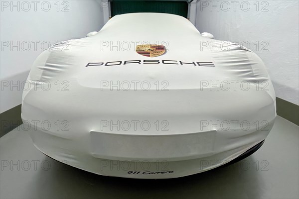 Perspective dynamic photo of sports car Porsche 911 Carrera in garage with protective cover indoor bonnet protective cover with on it logo company logo coat of arms lettering brand name