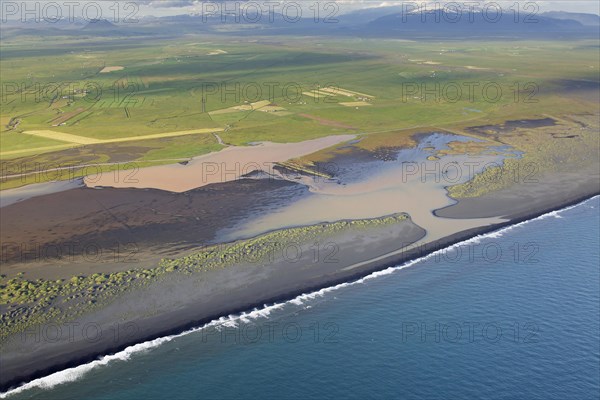 Aerial view over Landeyjarsandur showing beach with black volcanic sand and brown water laden with sediment flowing in sea in summer